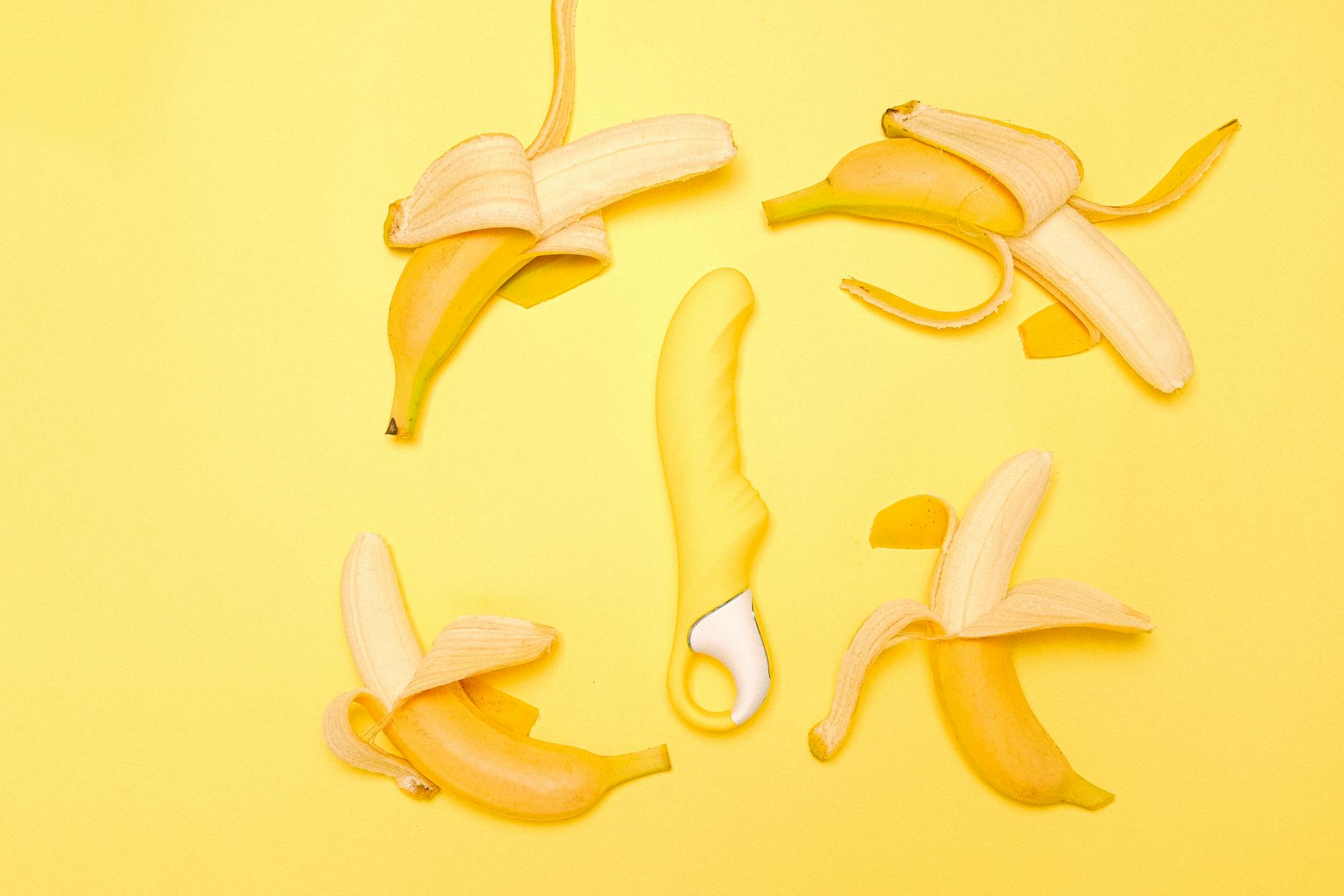 Yellow lemon vibrator surrounded by peeled bananas on yellow background