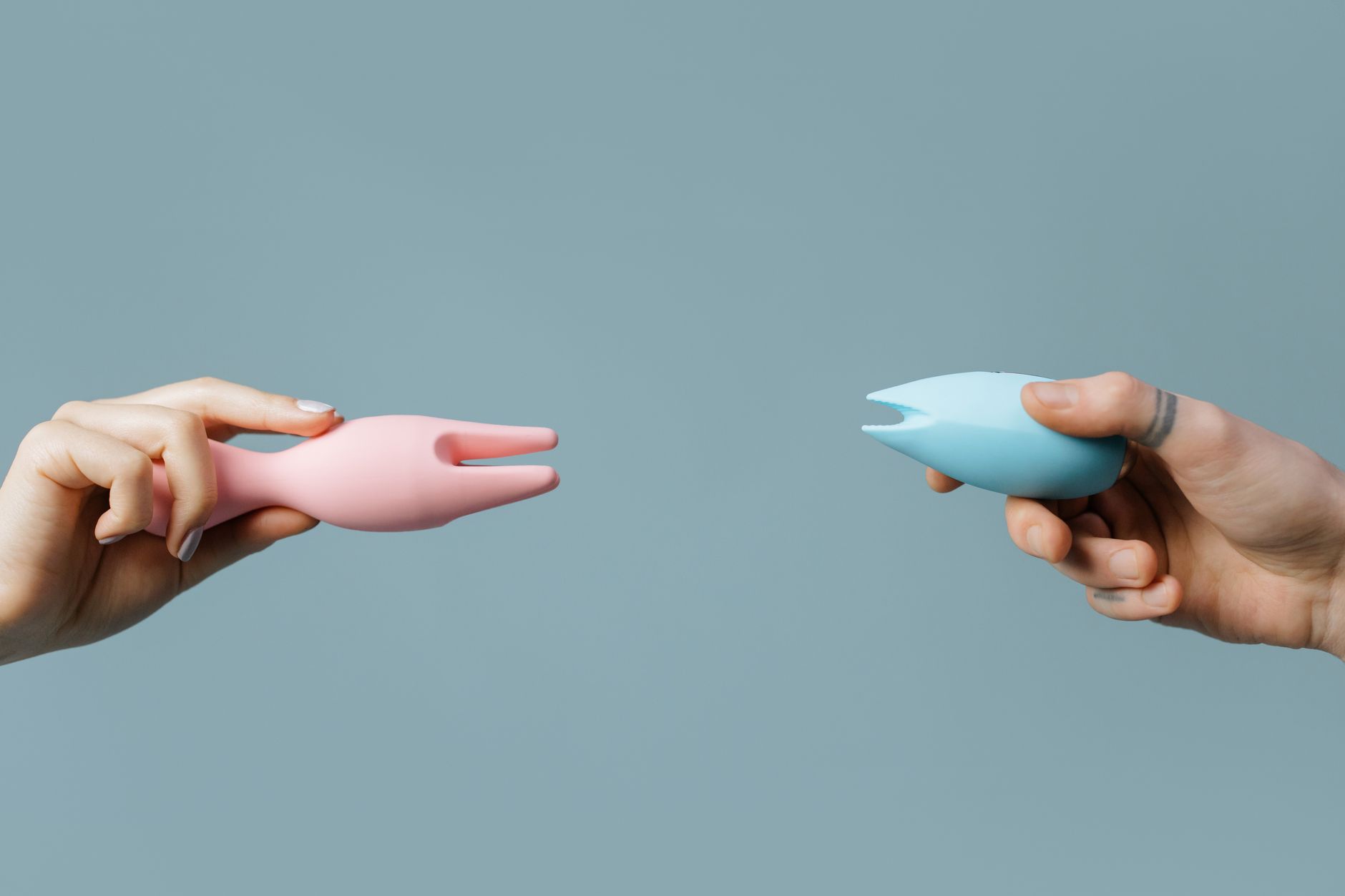 Hands holding pastel-colored silicone adult toys for intimate exploration