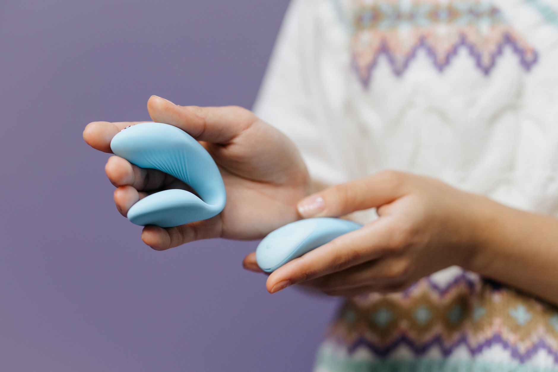 A hand holding a sleek blue vibrator against a purple background, ready for intimate use.
