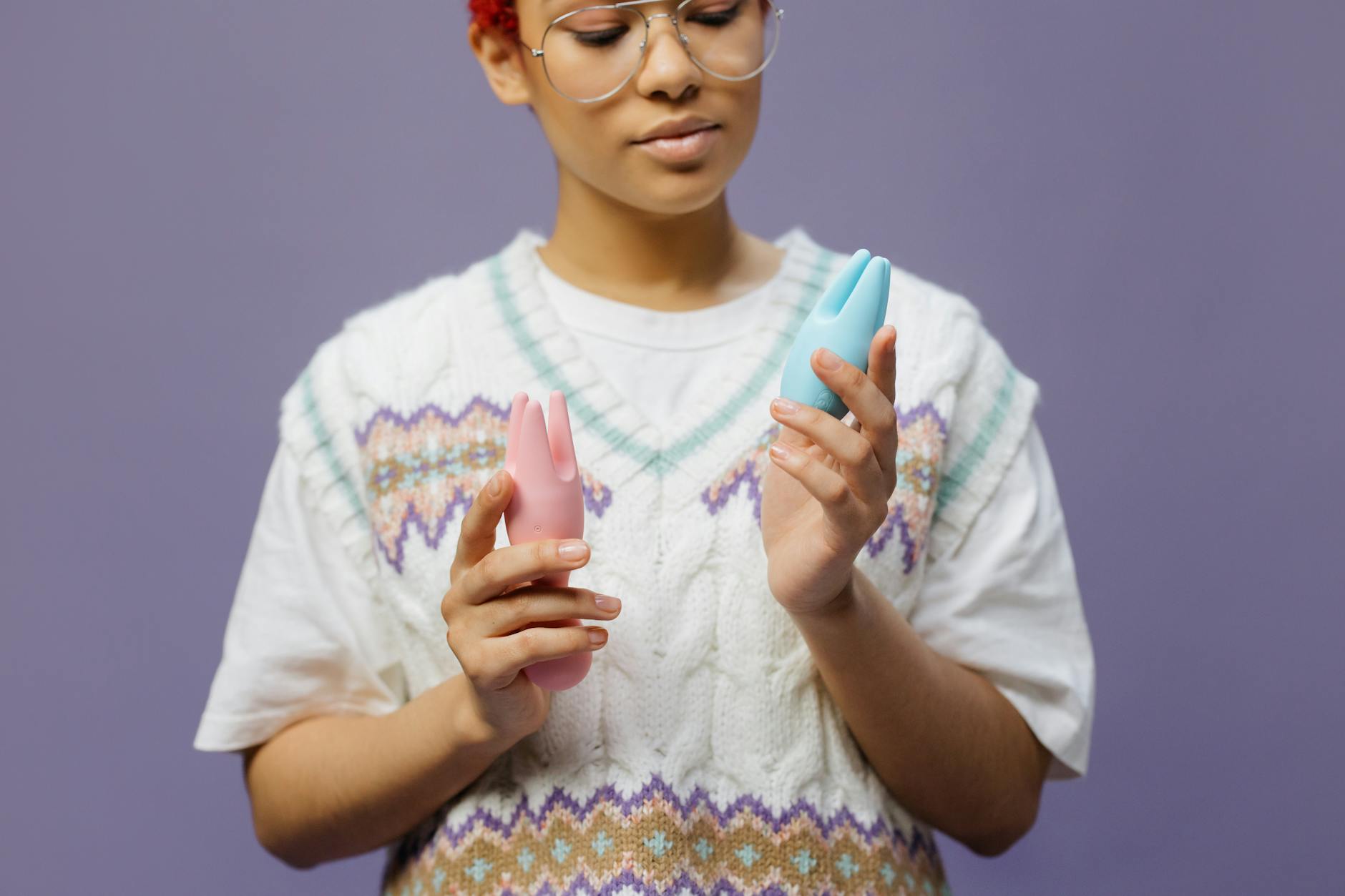 Woman holding colorful vibrators thoughtfully against purple background