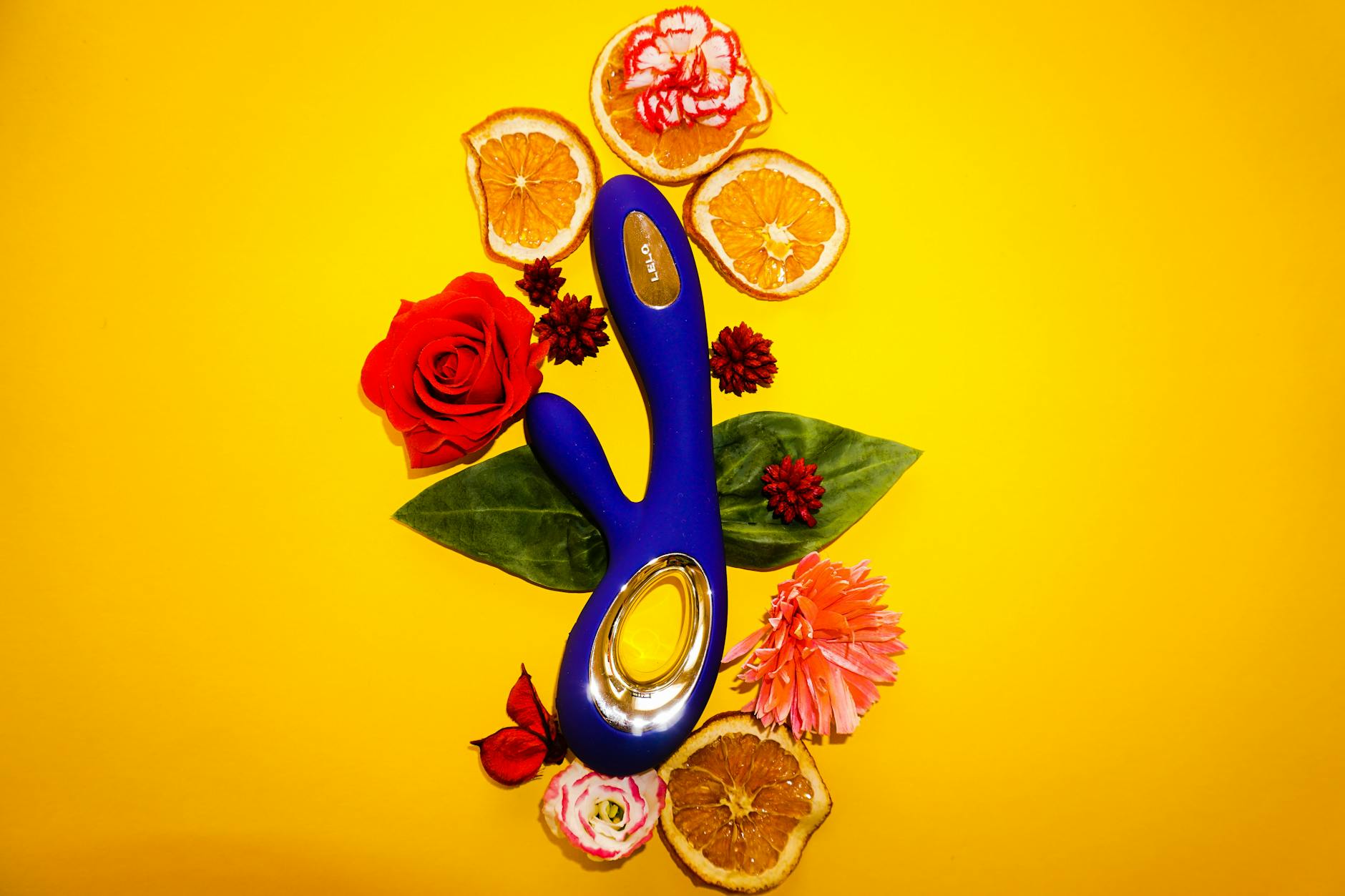 A blue vibrator surrounded by fresh lemons and flowers on a bright yellow background
